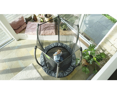 Enfant sur un trampoline de jardin rond avec filet de sécurité dans une véranda