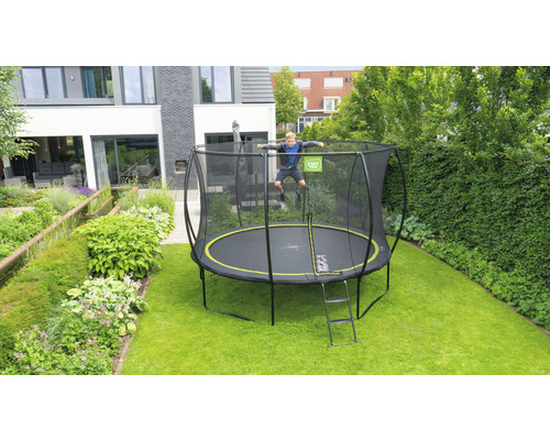 Junge springt auf einem Gartentrampolin mit Sicherheitsnetz und Leiter vor einem Wohnhaus.