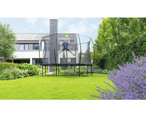 Junge springt auf einem Gartentrampolin mit Sicherheitsnetz und Leiter vor einem Haus