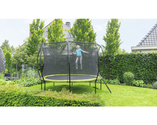 Une fille saute sur un trampoline de jardin avec filet de sécurité dans un jardin verdoyant.