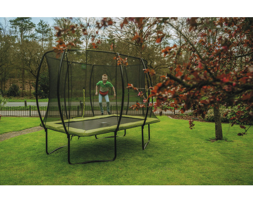 Garçon sautant sur trampoline de jardin rectangulaire avec filet de sécurité sur pelouse.