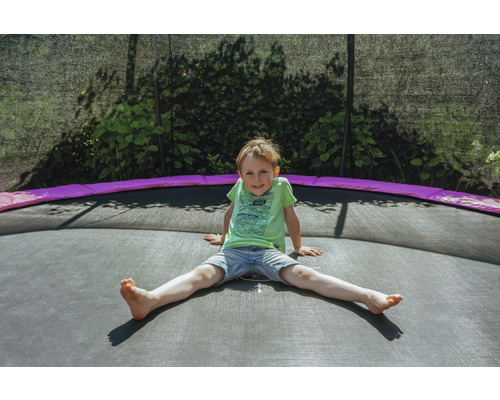 Un garçon est assis sur un trampoline de jardin.