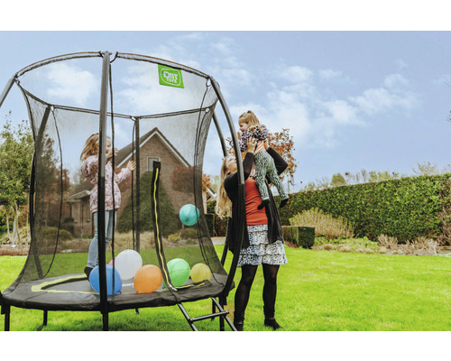 Trampoline avec filet de sécurité dans le jardin avec des enfants qui jouent et une femme portant un enfant sur ses épaules