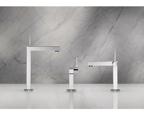 Trois robinets de lavabo modernes en métal devant un mur de marbre.