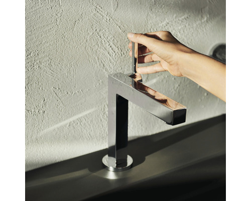 Une personne actionne un mitigeur de lavabo métallique au design angulaire.