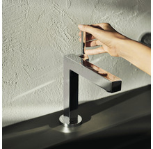 Une personne actionne un mitigeur de lavabo chromé et anguleux.