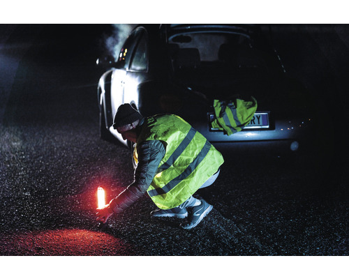 Une personne portant un gilet de sécurité place un voyant d''avertissement derrière une voiture sur la route.