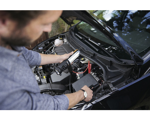 Une personne utilise une lampe de travail LED pour inspecter le compartiment moteur d''une voiture.