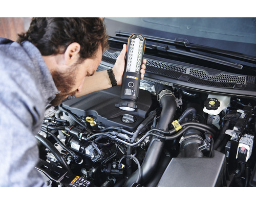Un homme éclaire un moteur de voiture avec une lampe de poche Worx