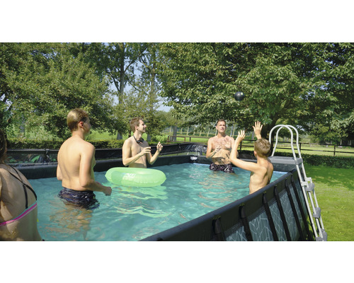 Une famille joue dans la piscine hors sol avec un ballon et une bouée dans le jardin.