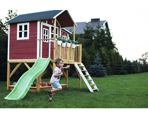 Enfant jouant devant une cabane rouge avec toboggan et échelle dans le jardin