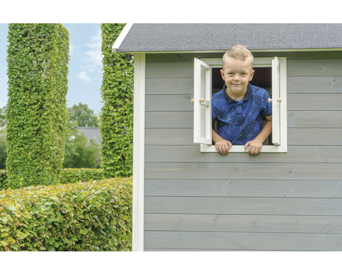 Un enfant regarde par la fenêtre d''une cabane en bois dans le jardin.