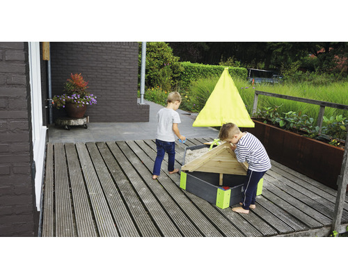 Deux enfants jouent dans un bac à sable avec un toit sur une terrasse en bois.