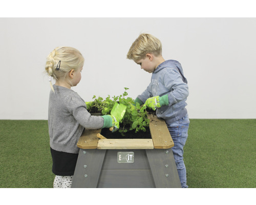 Zwei Kinder spielen mit einem Hochbeet im Garten.