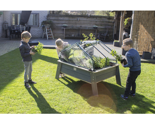 Trois enfants plantent un potager surélevé avec un dôme de forçage dans le jardin.