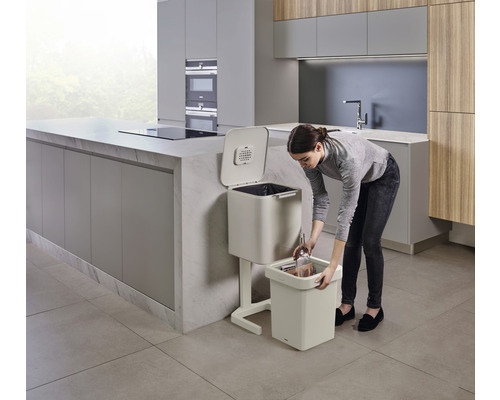 Femme vide des déchets organiques dans un seau à bokashi dans une cuisine.