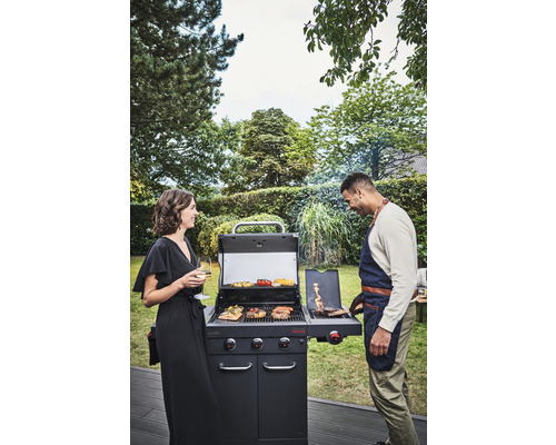 Grillszene im Freien mit einem Paar an einem Gasgrill, auf dem verschiedene Speisen zubereitet werden