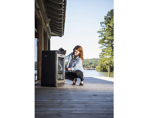 Une femme est accroupie devant un fumoir sur une terrasse en bois au bord d''un lac