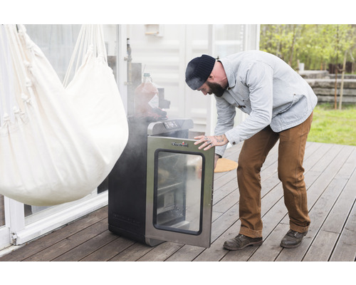 Un homme ouvre un fumoir électrique de la marque Char-Broil sur une terrasse.
