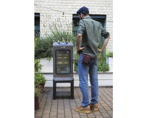 Un homme regarde un fumoir électrique dans le jardin.