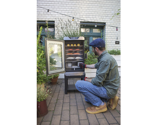 Un homme utilise un fumoir électrique dans le jardin avec de la nourriture à l''intérieur