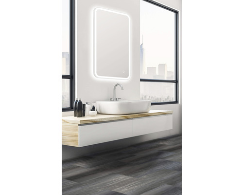 Salle de bains avec miroir lumineux, lavabo et meuble bas devant une fenêtre.