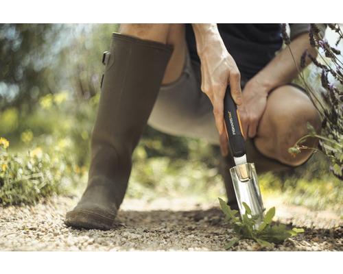 Scène de jardinage avec une personne portant des bottes en caoutchouc et utilisant une truelle de jardin Fiskars