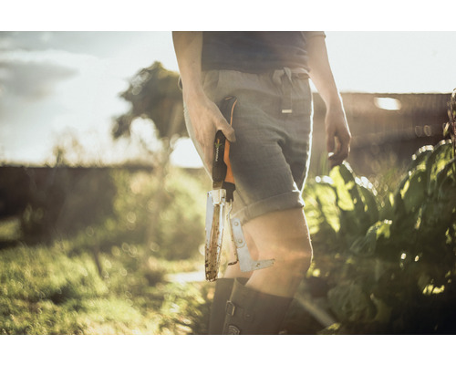 Une personne dans le jardin tient un désherbeur de la marque Fiskars.