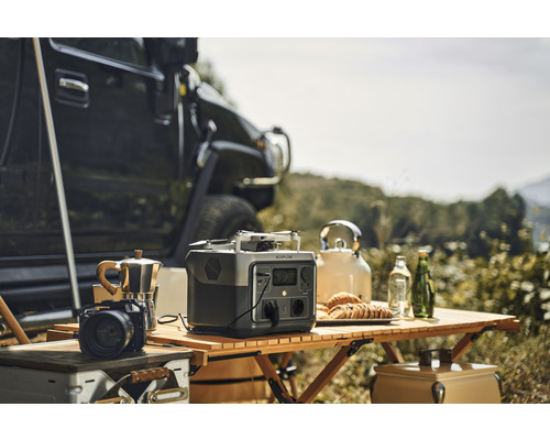 Scène avec une centrale électrique portable Ecoflow, une cafetière, un appareil photo, un drone et une bouilloire sur une table en bois à l''extérieur