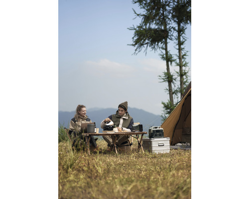 Deux personnes en camping avec table, chaises, ustensiles de cuisine et tente dans la nature