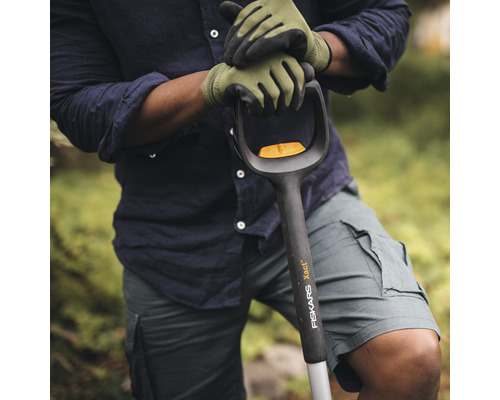 Eine Person mit Gartenhandschuhen hält einen Spaten der Marke Fiskars.