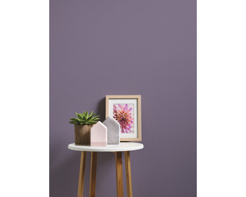 Dekorative Szene mit Topfpflanze, Hausdekorationen und einem gerahmten Bild auf einem kleinen Tisch vor einer Wand