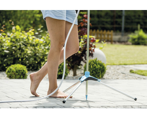 Frau steht barfuß neben einer Gartendusche auf einer Terrasse
