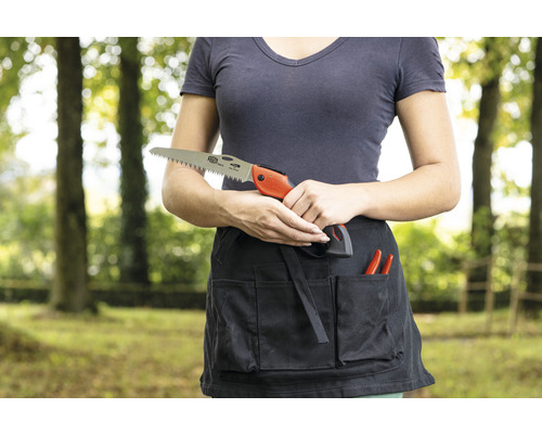 Une femme tient une scie à main devant un tablier de jardinage