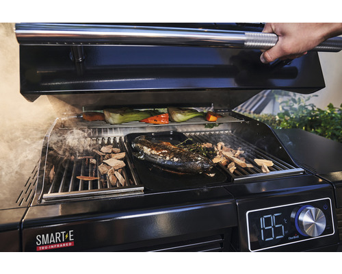 Ein schwarzer Grill mit Fisch, Gemüse und Räucherholz wird gegrillt.