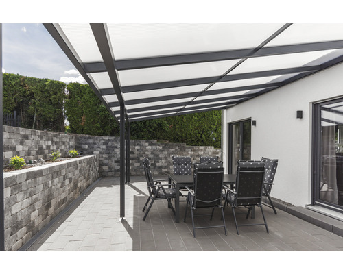 Terrasse mit Terrassenüberdachung, Gartentisch und Stühlen vor einer Steinmauer
