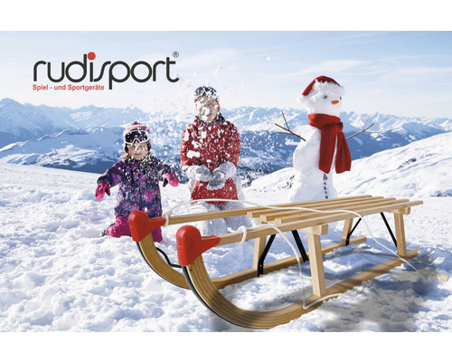 Holzschlitten vor Schneelandschaft mit spielenden Kindern und Schneemann