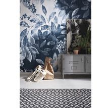 Raumansicht mit Blumentapete, Metallschrank, Gemälde, Zimmerpflanzen und Teppich mit geometrischem Muster