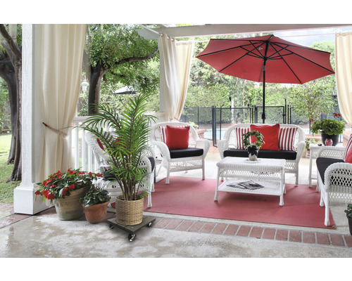Terrassenszene mit weißen Korbmöbeln, rotem Sonnenschirm und Topfpflanzen