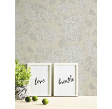 Tapete mit Blumenmuster, zwei Bilderrahmen mit den Aufschriften Liebe und Atmen, Topfpflanze und Limetten auf einem Tisch