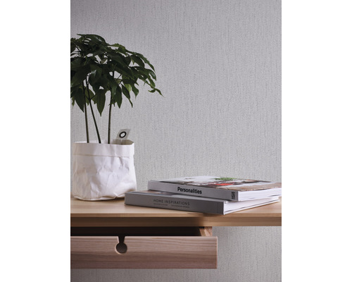 Nahaufnahme einer hellen Wandtapete mit Pflanze, Büchern und einem Tisch mit Schublade