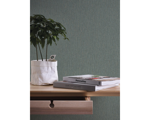 Nahaufnahme eines Tisches mit geöffneter Schublade, darauf Bücher und eine Pflanze vor einer strukturierten Tapete.