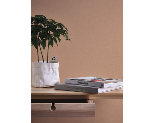 Dekorative Zimmerpflanze in weißem Papierkorb auf einem Tisch mit Dekorationsbüchern.