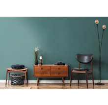 Wohnzimmer-Interieur mit Holzkommode, Stuhl, Stehlampe und Dekoration auf Parkettboden vor farbiger Wand