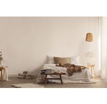Hell gestalteter Schlafbereich mit Bett, Holzhocker, Lampe und dekorativen Elementen für eine freundliche Atmosphäre