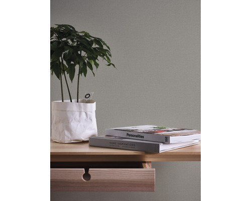 Nahaufnahme eines Tisches mit Pflanze, Büchern und offener Schublade vor einer strukturierten Wand