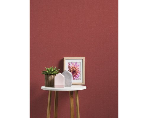 Dekorative Szene mit Pflanze, Deko-Häusern und Bilderrahmen auf einem Beistelltisch vor einer roten Wand