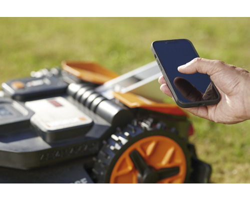 Ein Mann bedient einen Mähroboter mit einem Smartphone.