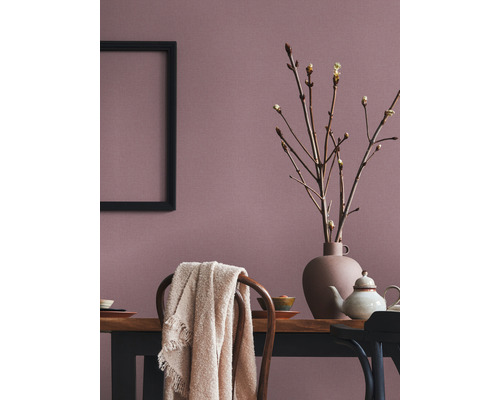 Esszimmer mit Holztisch, Geschirr, Vase mit Zweigen, Decke auf Stuhl und einem schwarzen Rahmen an der Wand.