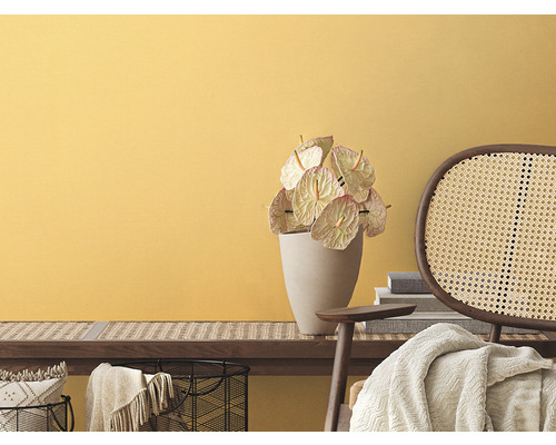 Wohnraum mit gelber Wand, Bank mit Rattangeflecht, Anthurien in Vase und Rattanstuhl